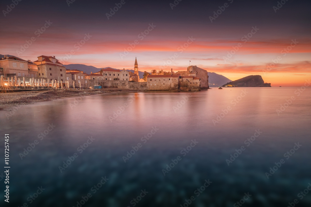 Obraz premium Colorful sunrise over Budva old town and Sveti Nikola island reflecting on Adriatic sea, Montenegro