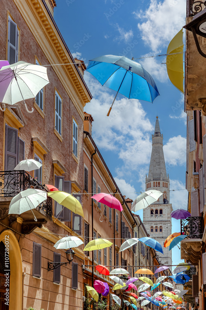 A delightful display of colorful umbrellas hangs gracefully over a quaint street in Modena, Italy, adding character and charm to the lively town atmosphere.