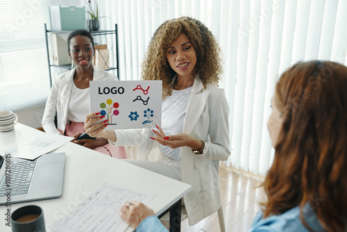 Businesswoman presenting a creative logo design concept during meeting with colleagues in modern office setting. Focus on teamwork and innovative project ideas photo