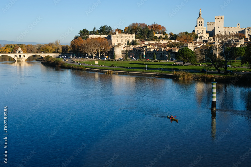 Scenic view of Avignon. The kayak is visible on the Rhône River in the foreground. On the left is the Saint-Bénézet Bridge (Pont d'Avignon). On the right is Palais des Papes (Palace of the Popes). Scenic view of Avignon. The kayak is visible on the Rhône River in the foreground. On the left is the Saint-Bénézet Bridge (Pont d'Avignon). On the right is Palais des Papes (Palace of the Popes).