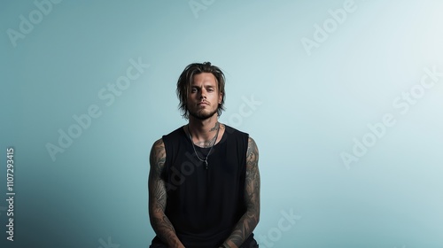 A rough heavy metal musician with tattoos sits calmly in a minimalistic, isolated space, showcasing his intense presence and unique style as he engages in reflection and creativity. photo