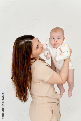 mom with a baby on a white isolated background and on the bed, a place for text, a young mother gently hugs her little baby girl, maternal love and care