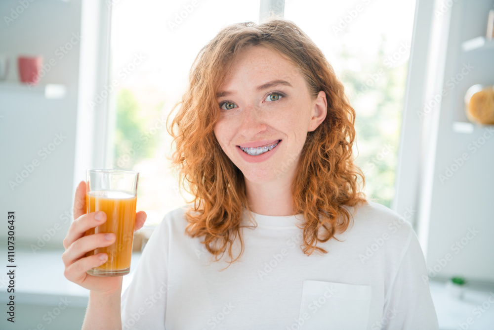 Young woman with red hair smiling brightly while enjoying a refreshing glass of orange juice in a sunlit kitchen. Young woman with red hair smiling brightly while enjoying a refreshing glass of orange juice in a sunlit kitchen.