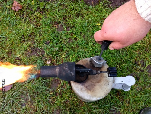 Macro photography of the process of pumping pressure into a gasoline blowtorch using a special pump that is built into the lamp body. The topic of a hand tool for treating surfaces with high temperatu photo