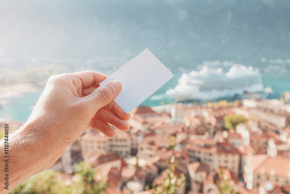Tourist holding empty ticket or business card with cruise ship and Kotor in background