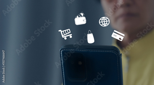 Young professional using a smartphone to shop online, illustrating digital commerce concepts with icons of wallet, cart, and shopping essentials in a modern environment.