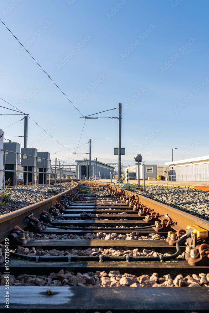 Naklejka premium Railway tracks converging into the distance under a clear blue sky