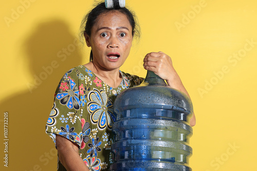 Indonesian Mom Holding a Five Gallon Bottle of Mineral Water, Isolated on Yellow Background photo