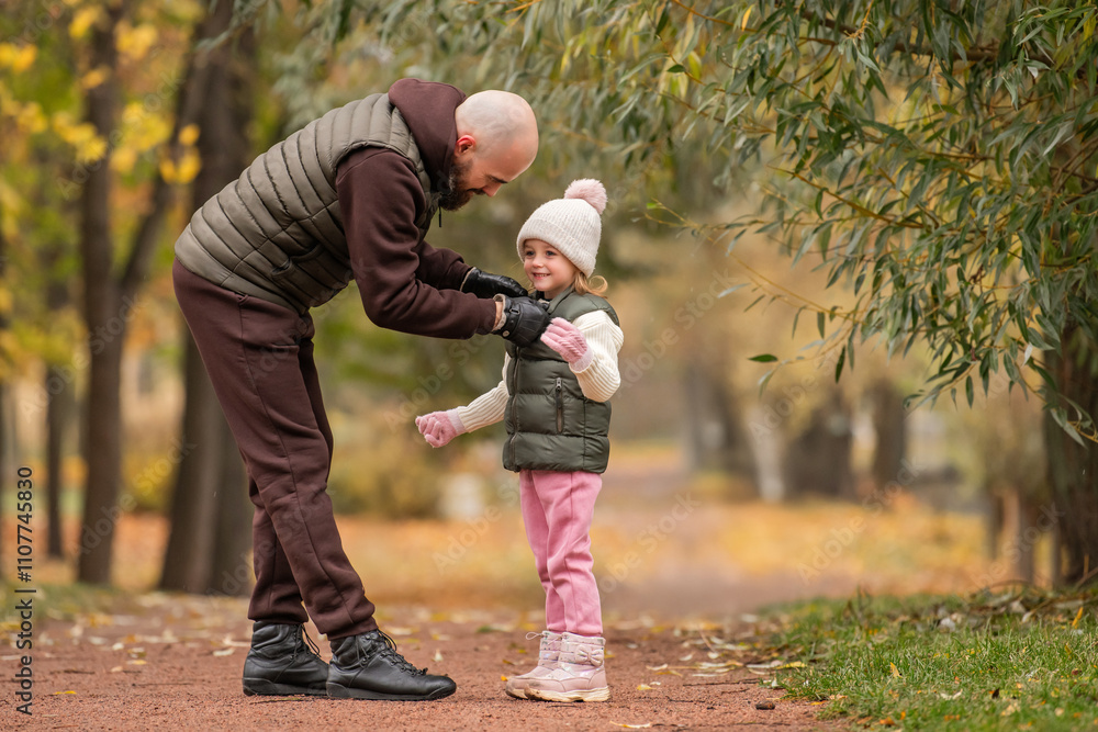 Fototapeta premium happy father carefully adjusts the zipper on his little daughter's jacket during a walk in an autumn park.