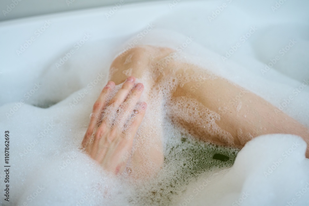 Fototapeta premium Medium close up of unrecognizable female body covered with white foam, woman resting in bathtub