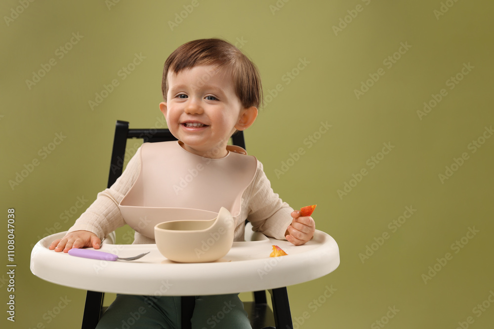 Cute little baby eating healthy food from bowl in high chair on olive background, space for text Cute little baby eating healthy food from bowl in high chair on olive background, space for text