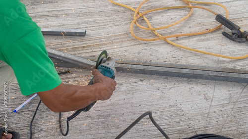 A worker hands are holding and using a tool to cut steel until it sparks in a construction site.