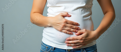 Girl with bloated stomach and hand on her belly, looking uncomfortable, after overindulging in unhealthy fatty foods on a grey background._00001_