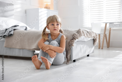 Orphanage concept. Sad little girl sitting on floor in child`s room photo