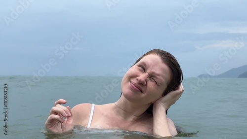 woman suffers from water getting into her ear in the sea during swimming
