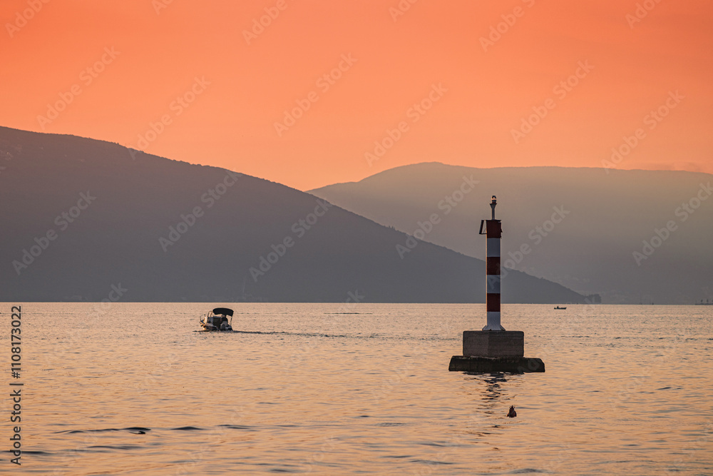 Fototapeta premium Small motorboat sailing near a cardinal mark at sunset with mountains in the background