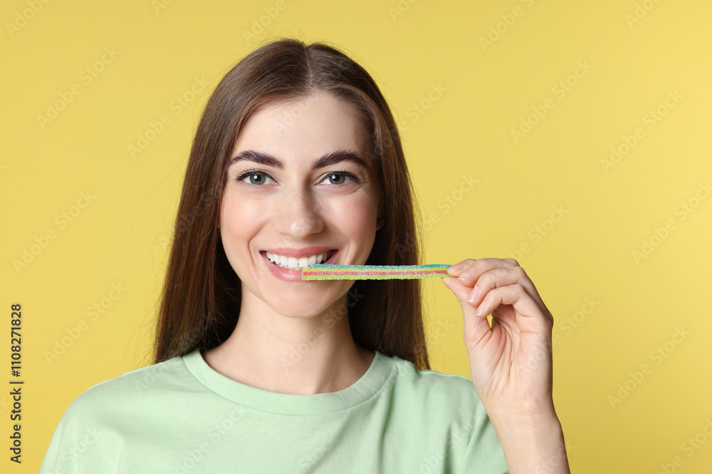 Young woman eating tasty rainbow sour belt on yellow background Young woman eating tasty rainbow sour belt on yellow background