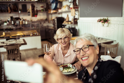 Two smiling senior female friends taking selfie at a restaurant photo