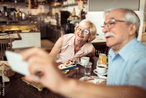 Happy senior couple taking selfie while eating at cozy bistro photo