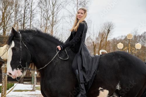 фотографія woman princess in black cloak sits astride black steed horse