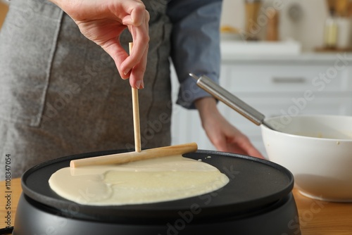 Woman cooking delicious crepe on electrical pancake maker in kitchen, closeup photo