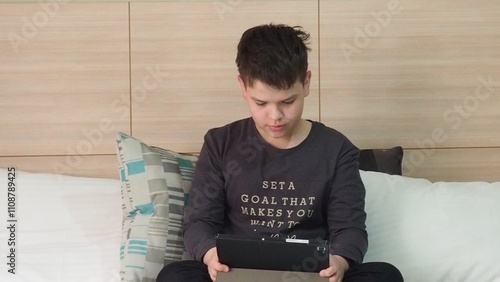 Smiling teenage school kid using tablet computer, relaxing on sofa at home, watching learning video, movie, online class, listening to music, communicates with friends, social networks