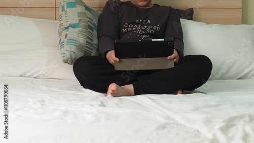 Smiling teenage school kid using tablet computer, relaxing on sofa at home, watching learning video, movie, online class, listening to music, communicates with friends, social networks