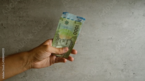 Hand holding chilean pesos against a concrete background