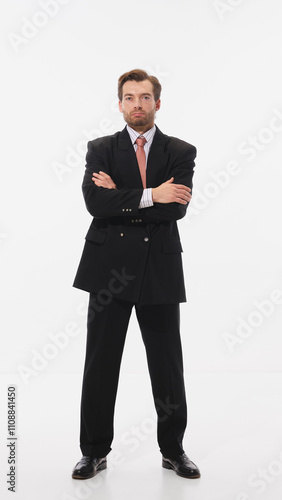 Stylish young man in black suit with red tie, standing confidently with arms crossed against white studio background. Concept of business, leadership, occupation, modern culture. Ad