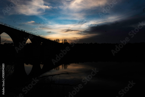 Silhouette of an Arched Bridge at Sunset Reflecting on Calm Waters in Fuentes Claras, Avila, CyL