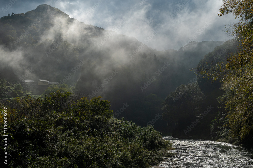 Fototapeta premium Misty mountain valley with a flowing river and forested hills in Shikoku, Japan.