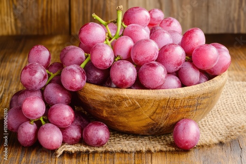 A collection of ripe red grapes is displayed in a wooden bowl on a rustic wooden surface, complemented by a burlap cloth photo