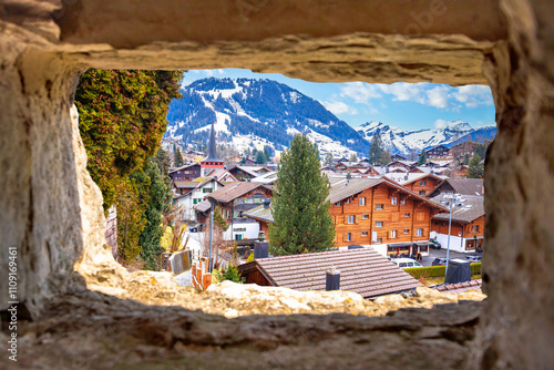 Idyllic Alpine village of Gstaad view through stone window, luxury winter destination