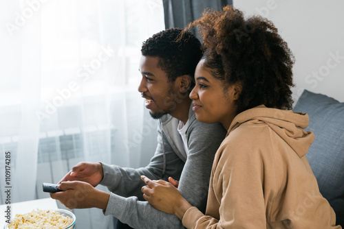 Canvas Print African American couple relaxes on a cozy sofa, sharing a joyful moment while watching a show with a bowl of popcorn
