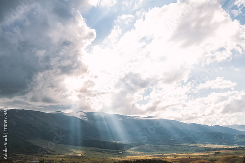 Sun rays breaking through clouds, illuminating a valley and mountains
