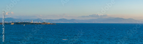 The image shows the Tarifa coastline in Spain, featuring a lighthouse on a rocky outcrop, kite surfers, and the distant mountains of Morocco across the Strait of Gibraltar.
