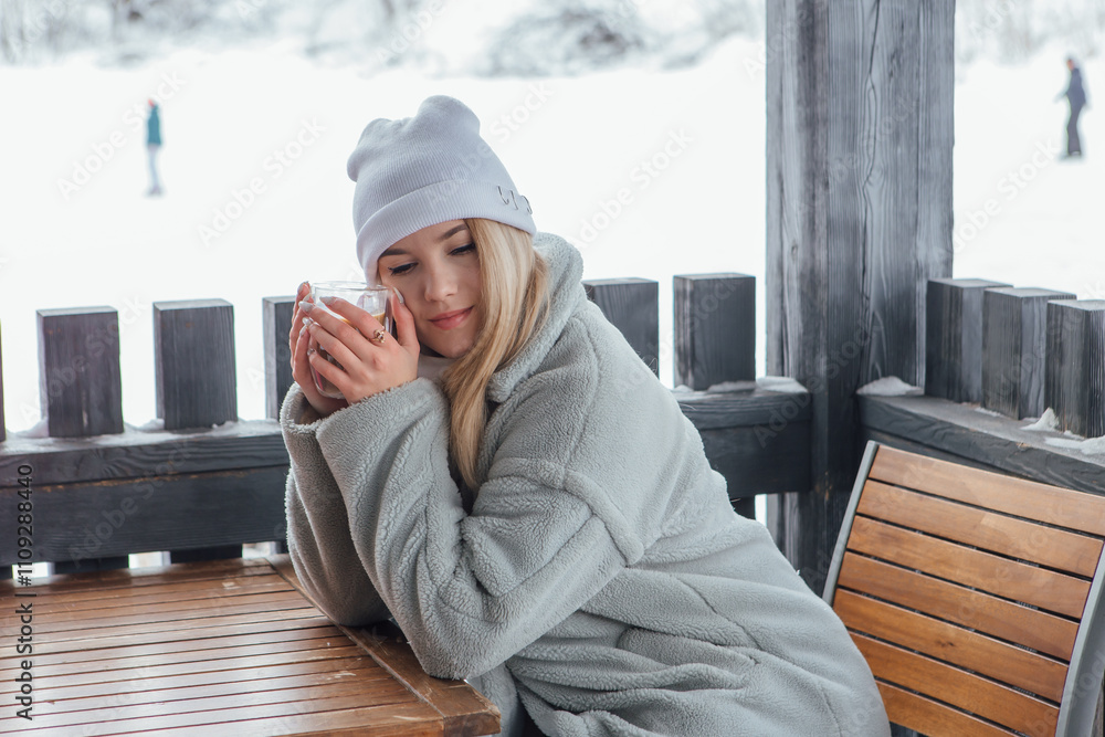A beautiful young girl smiling and enjoying drinking coffee outdoors in a winter day. A beautiful young girl smiling and enjoying drinking coffee outdoors in a winter day.