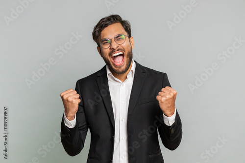 Happy joyful Indian businessman celebrating success victory, winning birthday, lottery jackpot goal achievement play game good positive news, triumph. Young Arabian man isolated on gray background photo