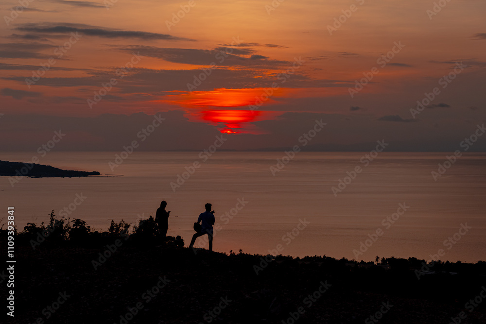 Fototapeta premium Silhouetted Figures Witnessing a Breathtaking Sunset by the Ocean