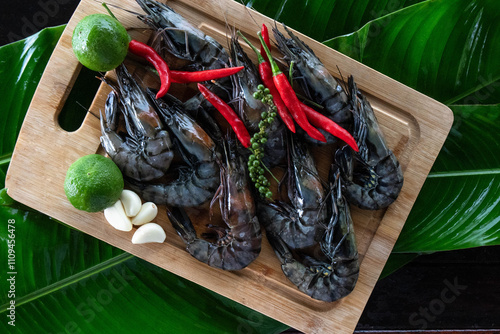 Freshly harvested tiger shrimp on vibrant banana leaves, accompanied by chilies, lime, and garlic, showcasing a delightful Asian culinary tradition. photo