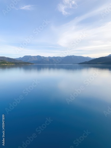 Tranquil lake with smooth blue water reflecting sky, surrounded by greenery and mountains, greenery, tranquil