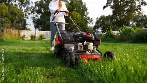 woman with lawnmower mows lawn in garden plot