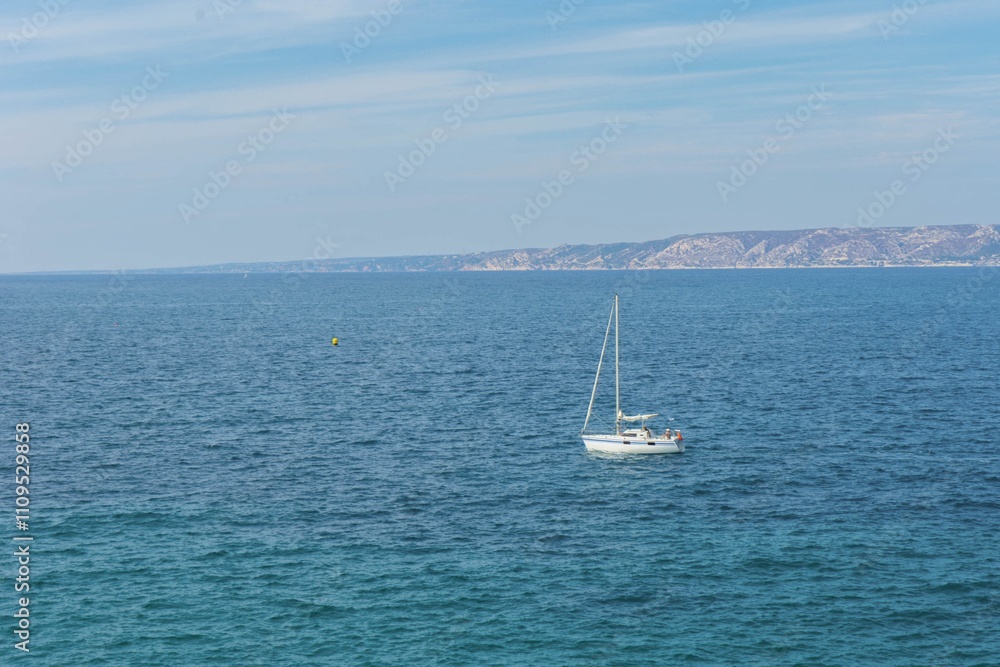 Serene ocean view with white sailboat on deep blue waters near coastal landscape Serene ocean view with white sailboat on deep blue waters near coastal landscape