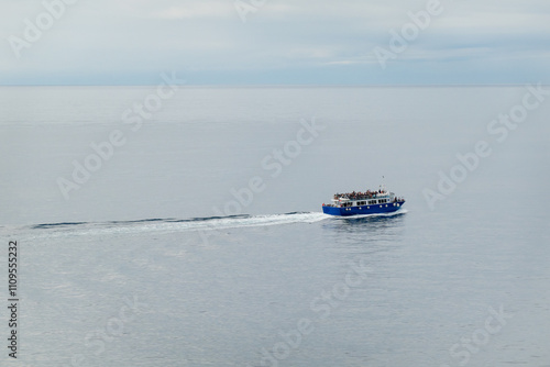 Blue ferry sails peacefully across calm open sea with scattered passengers onboard enjoying a serene journey. photo