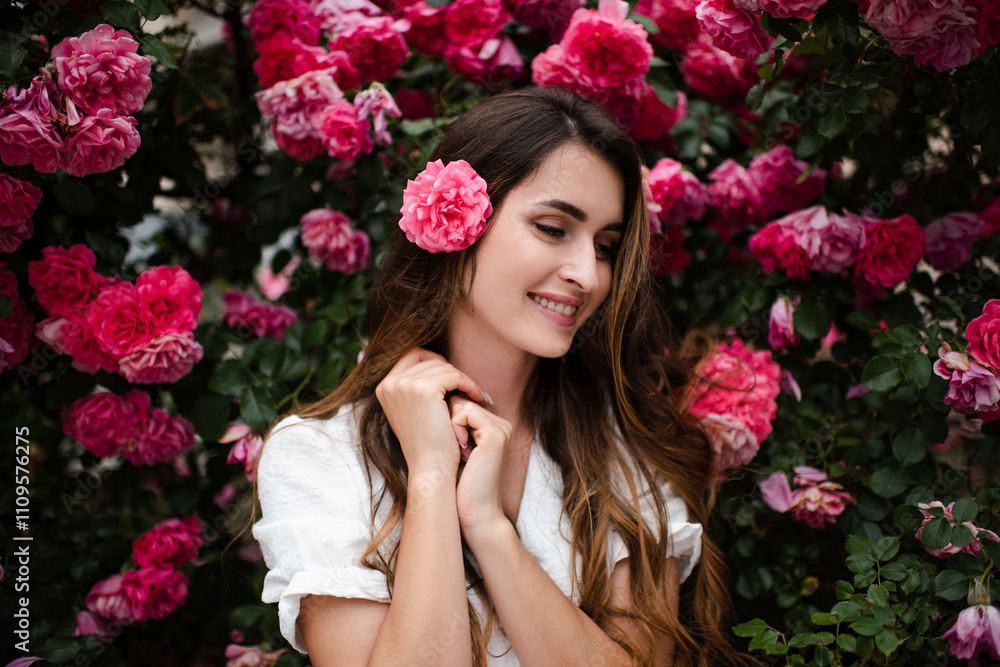 Beautiful young woman 25-29 year old with long blonde hair posing with pink rose flowers in garden outdoors. Springtime.