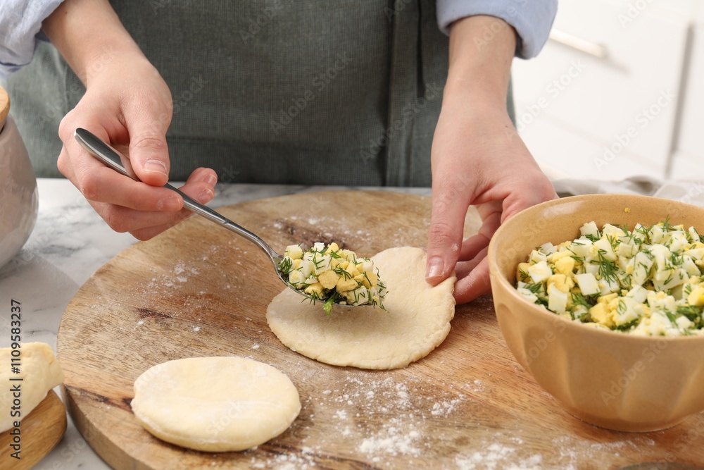 Woman making pirozhki (stuffed pastry pies) with eggs and dill at table indoors, closeup Woman making pirozhki (stuffed pastry pies) with eggs and dill at table indoors, closeup