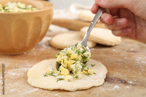 Woman making pirozhki (stuffed pastry pies) with eggs and dill at table, closeup photo