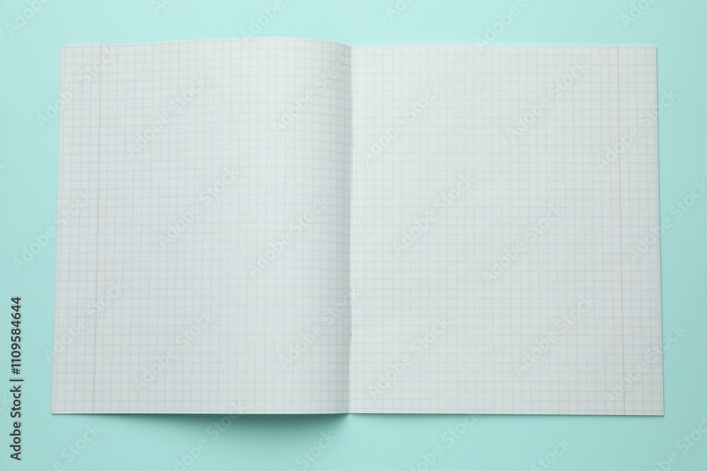Open copybook with checkered sheets of paper on light blue background, top view. School stationery Open copybook with checkered sheets of paper on light blue background, top view. School stationery