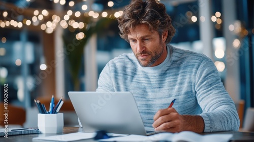 A man in a cozy sweater focuses on his work at a laptop, surrounded by a warmly lit modern office setup hinting concentration and creativity.