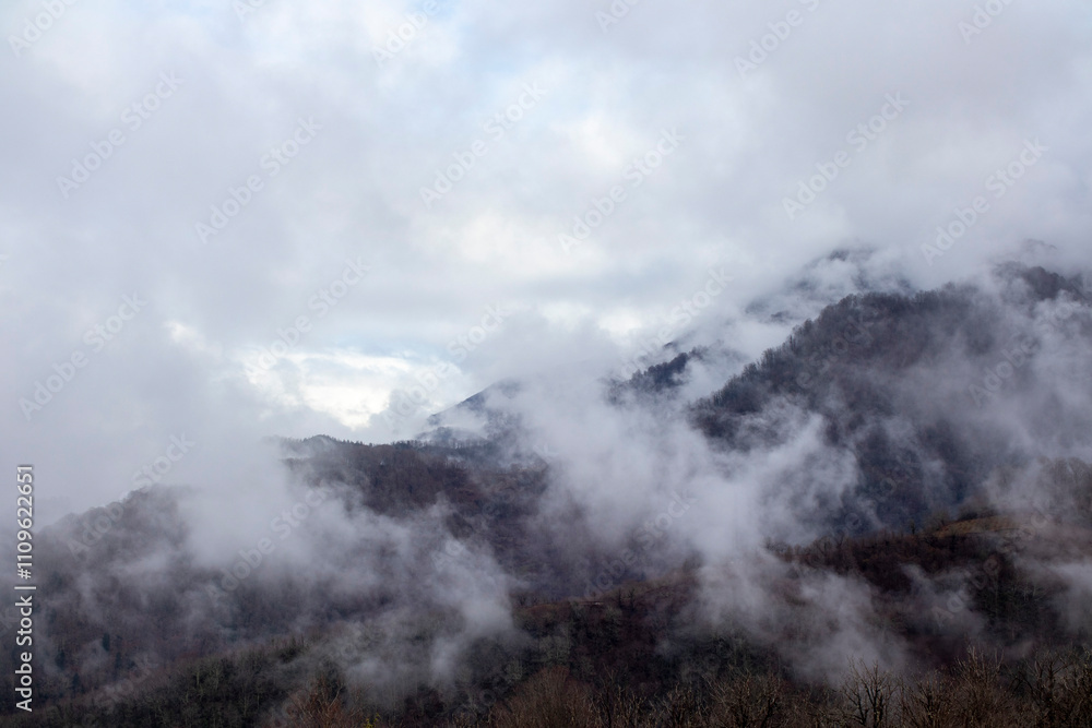 A majestic mountain is shrouded in fog and clouds on a gloomy day A majestic mountain is shrouded in fog and clouds on a gloomy day